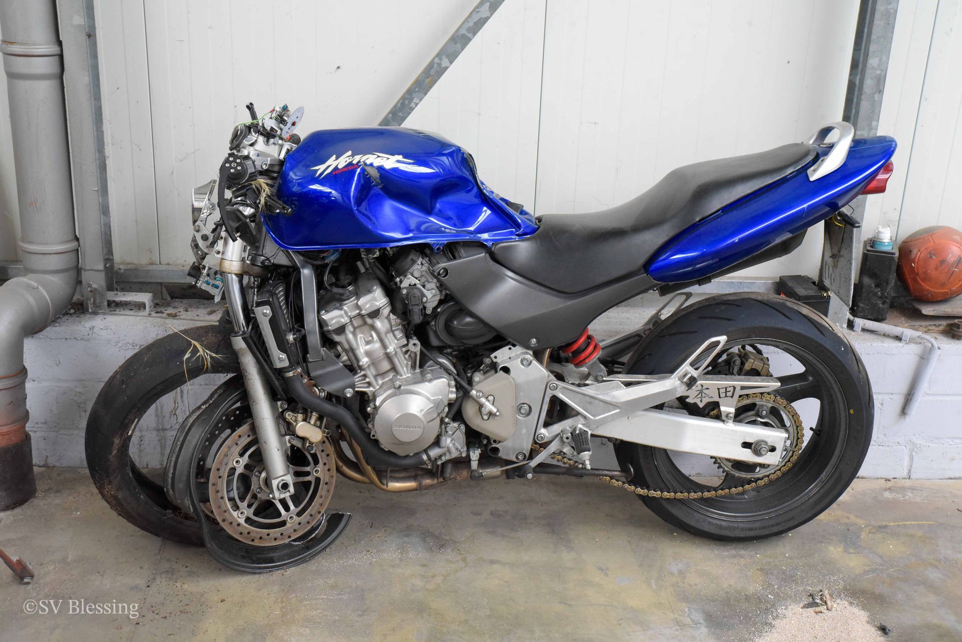 Ein blaues Motorrad mit einem kaputten Reifen steht in einer Garage