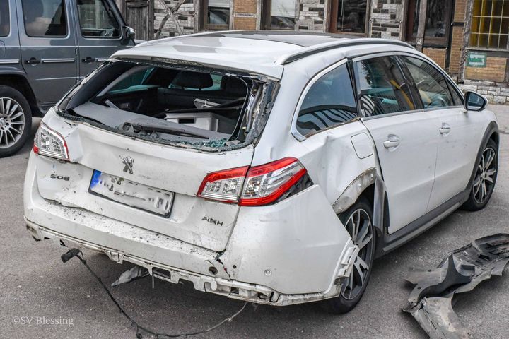 Ein weißes Auto mit einer kaputten Windschutzscheibe steht am Straßenrand.