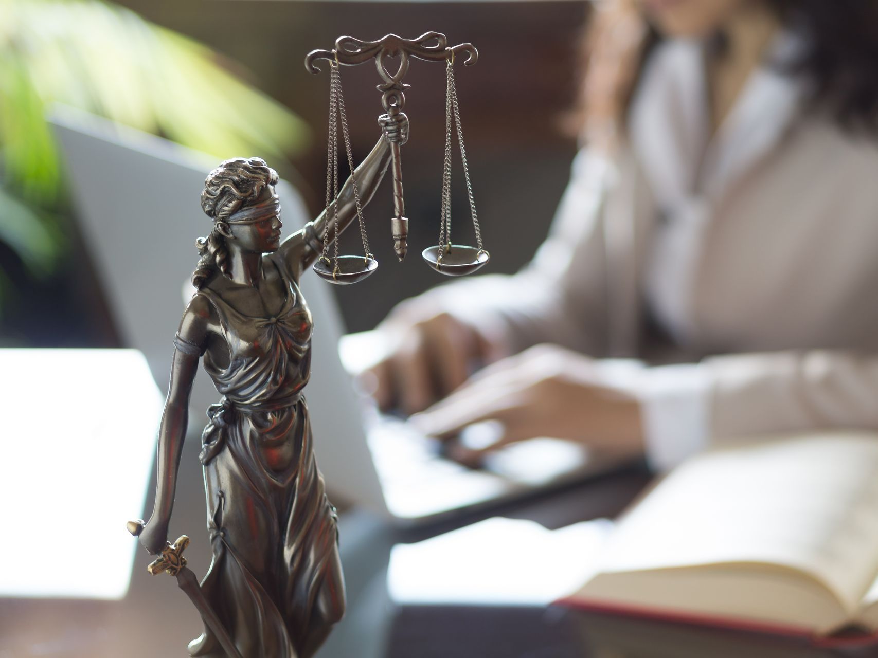 Statue de la justice en premier plan et une avocate devant son PC en arrière-plan.