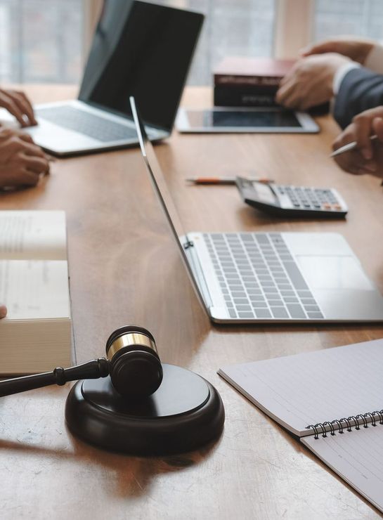 Plusieurs personnes assises autour d'une table avec des ordinateurs, des livres et le marteau de juge.