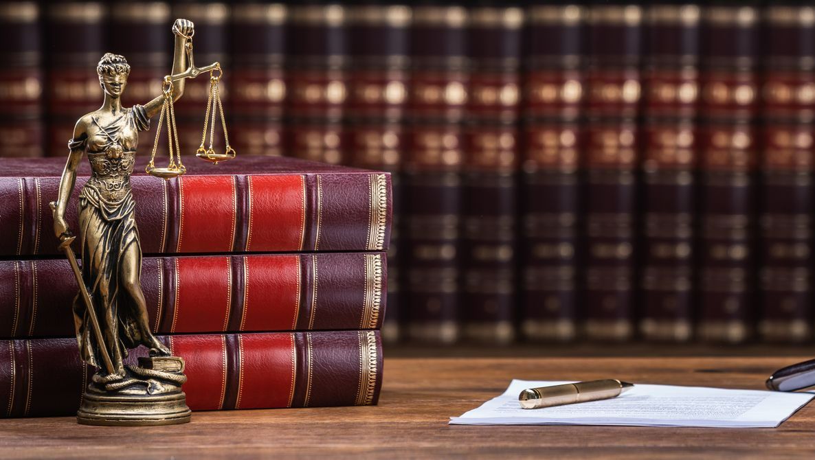Nombreux livres en arrière-plan et la statue de la justice avec le marteau de juge en premier plan.