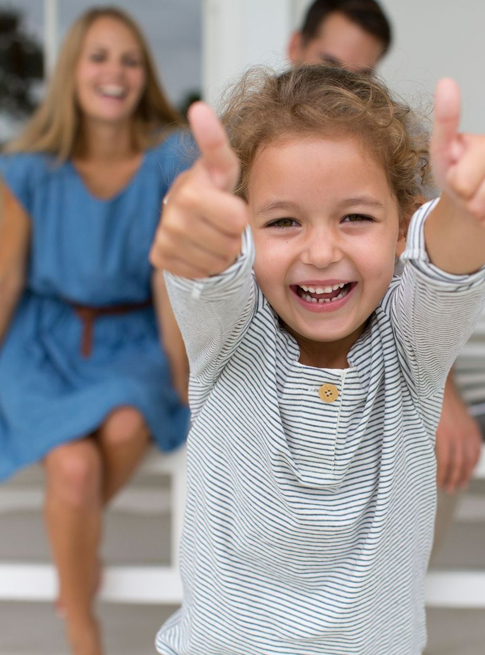 Une petite fille en premier plan et ses parents en arrière-plan.