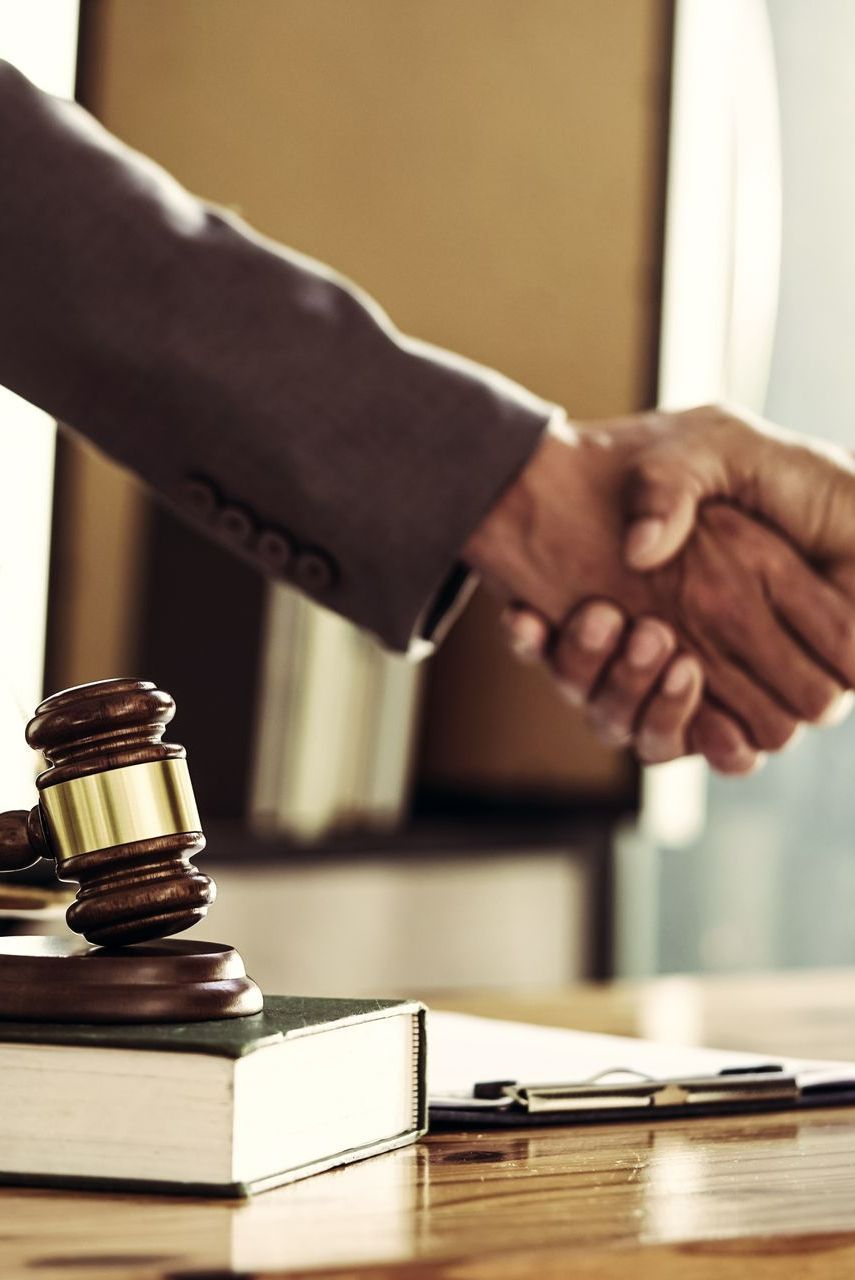 Deux personnes qui se serrent la main et le marteau de juge en premier plan.