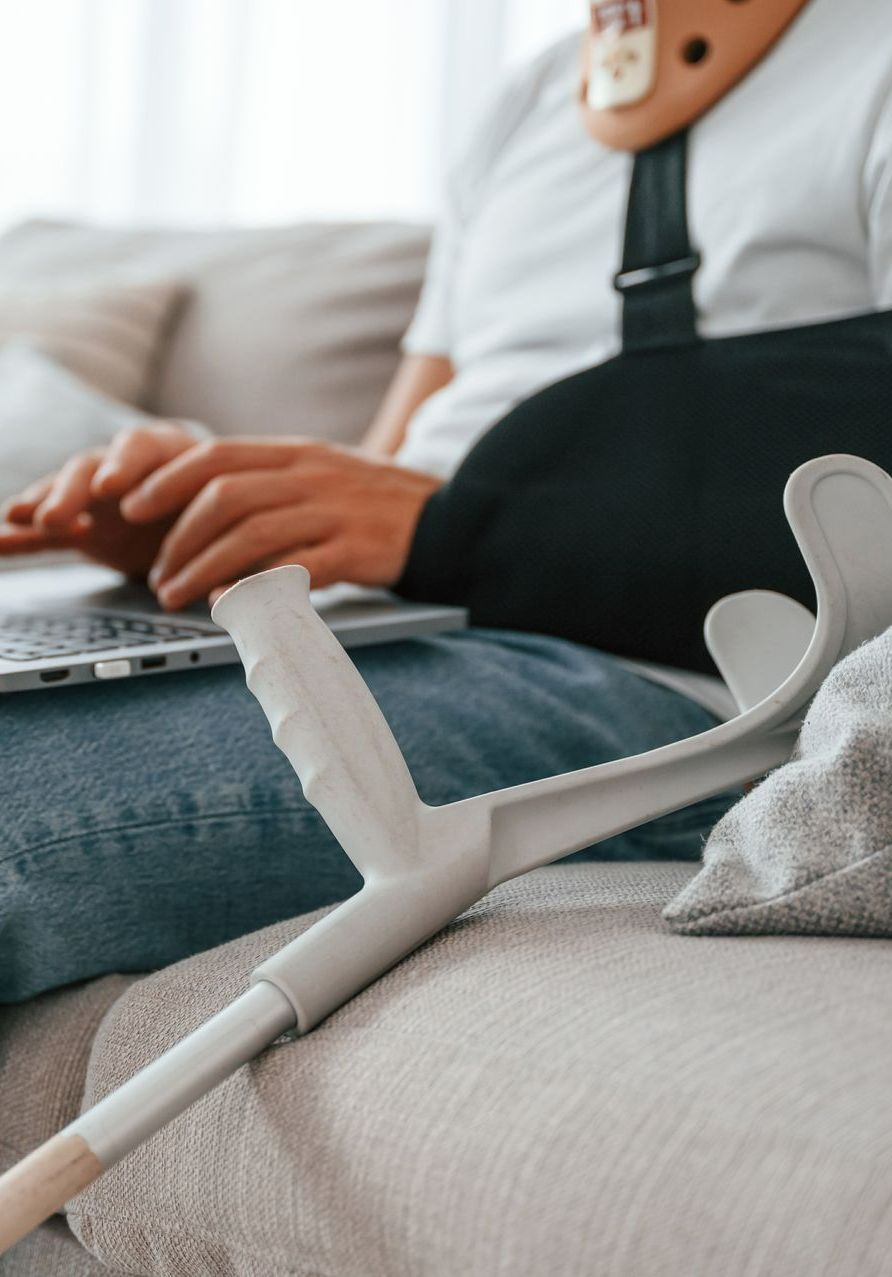 Une personne assise sur le canapé qui tient son PC et une béquille en premier plan.