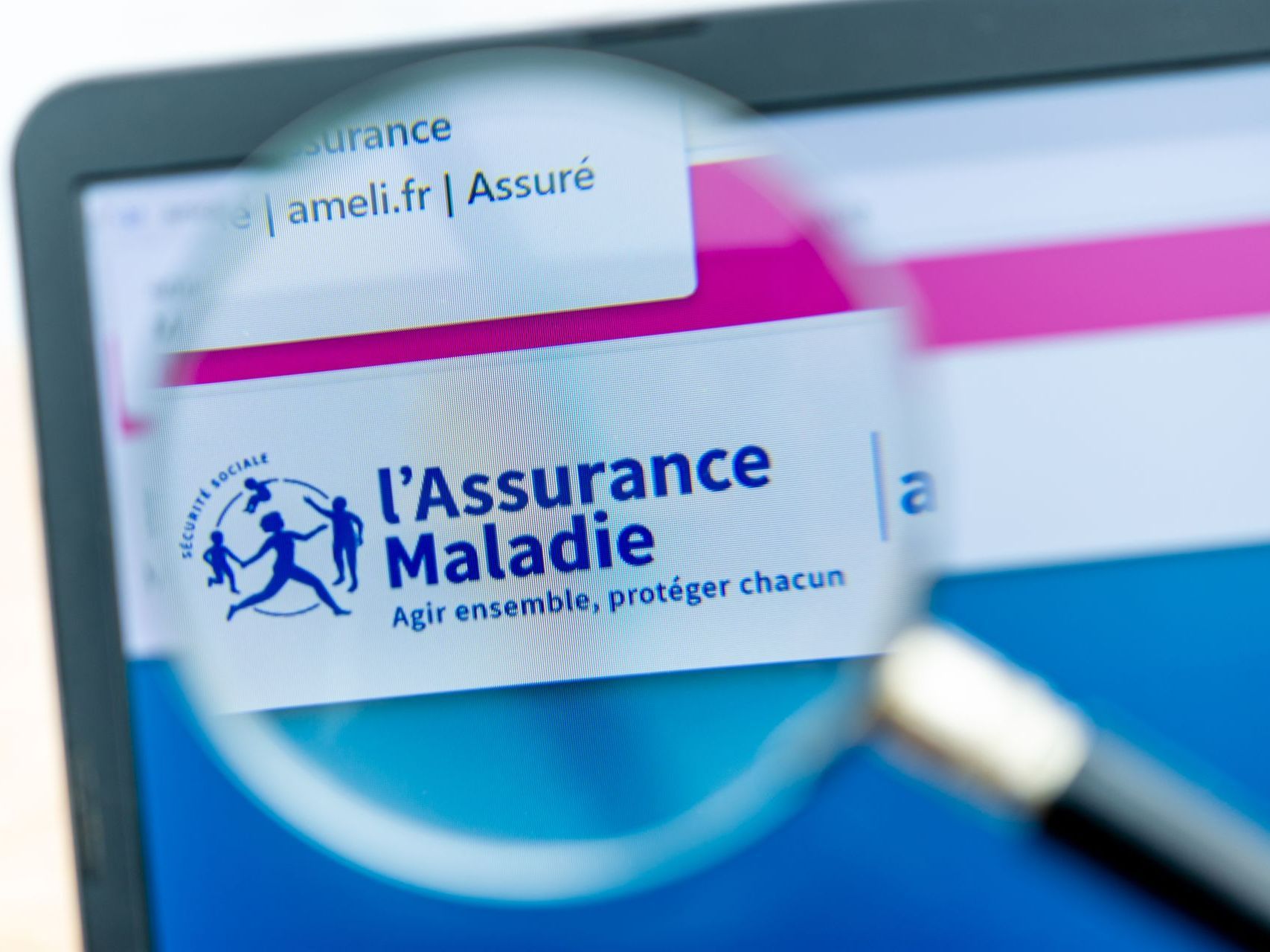 Gros plan sur une partie d'écran d'un ordinateur avec le logo de l'Assurance Maladie sous la loupe.