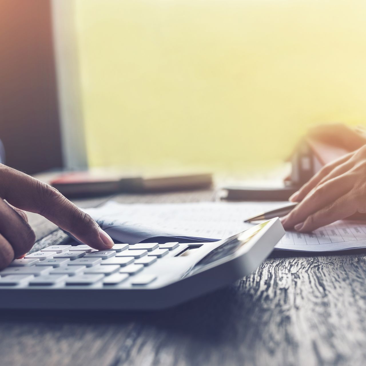 Une calculatrice en premier plan et une personne qui signe un document en arrière-plan.