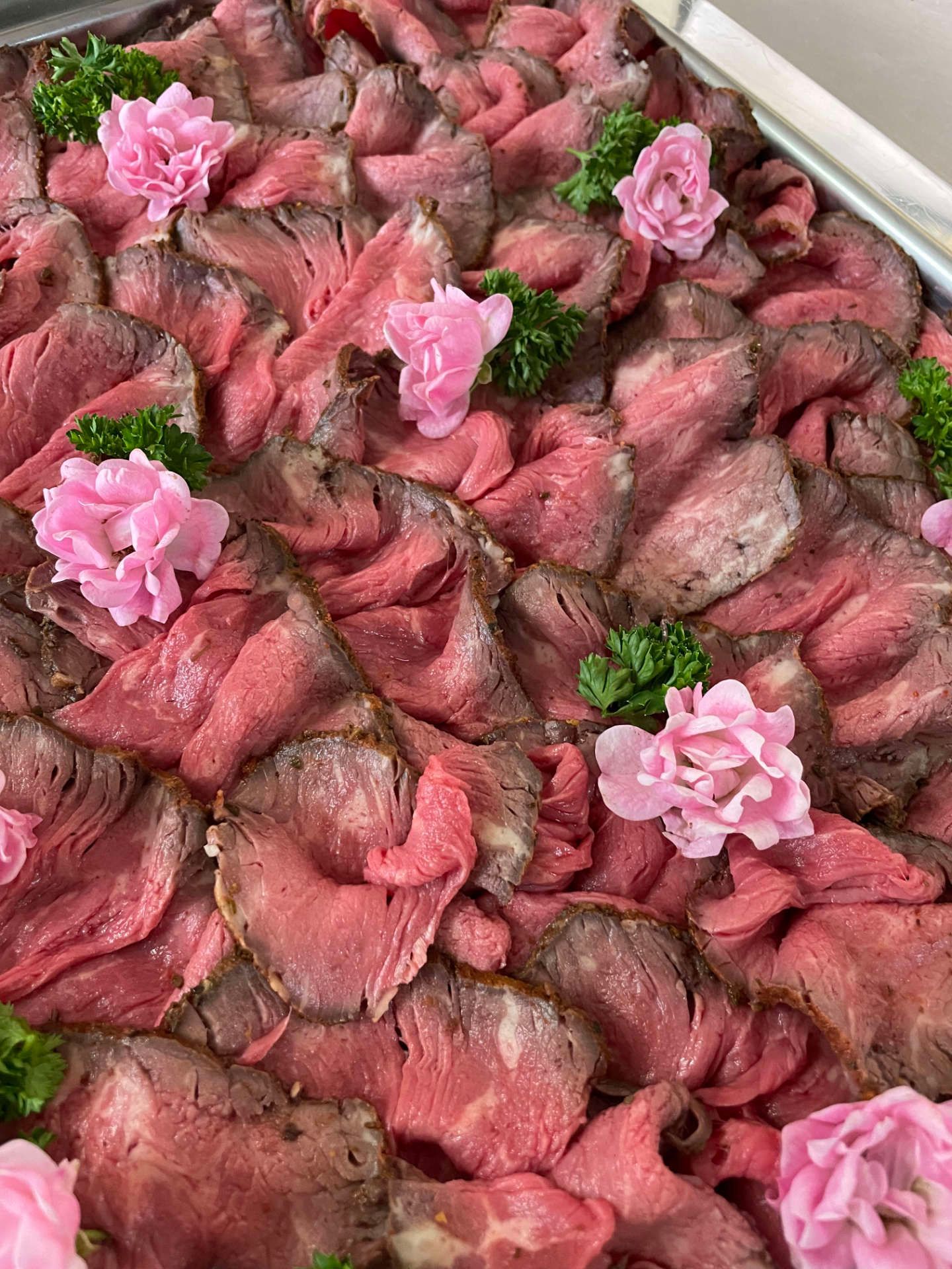 Eine Nahaufnahme eines Tabletts mit Roastbeef und rosa Blumen darauf.
