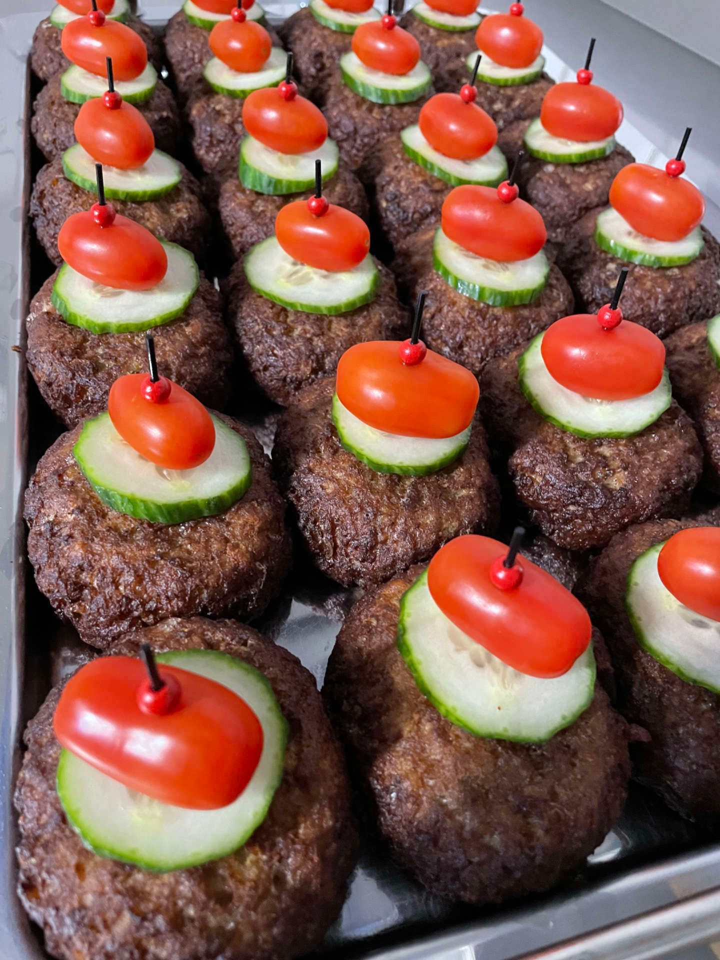 Ein Haufen Fleischbällchen mit Tomaten und Gurken obenauf