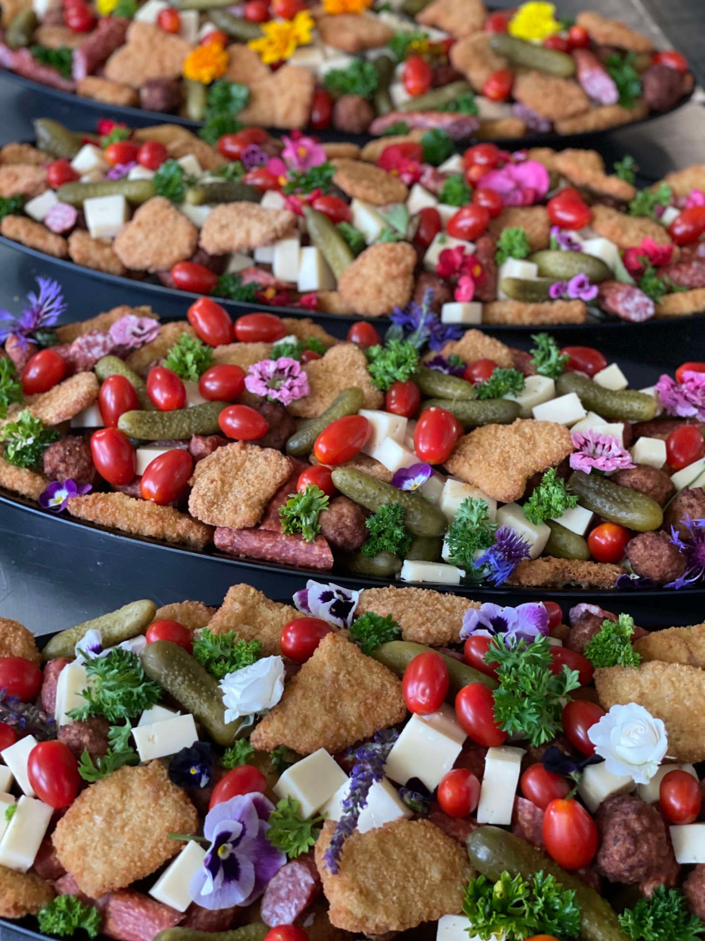 Drei Teller gefüllt mit Nuggets, Tomaten, Gurken, Käse und Blumen.