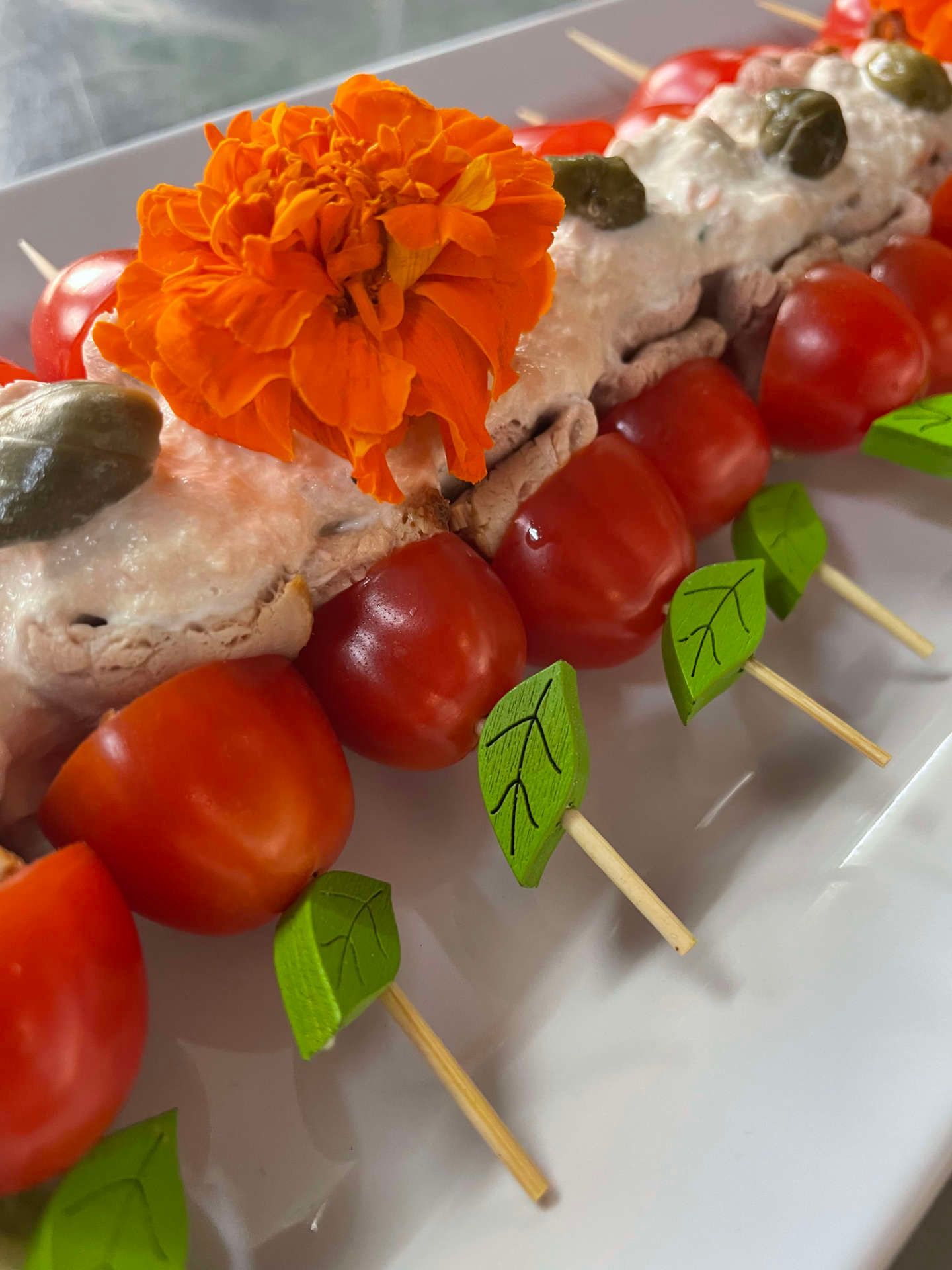 Ein weißer Teller, belegt mit Tomaten, Kapern und einer Blume.