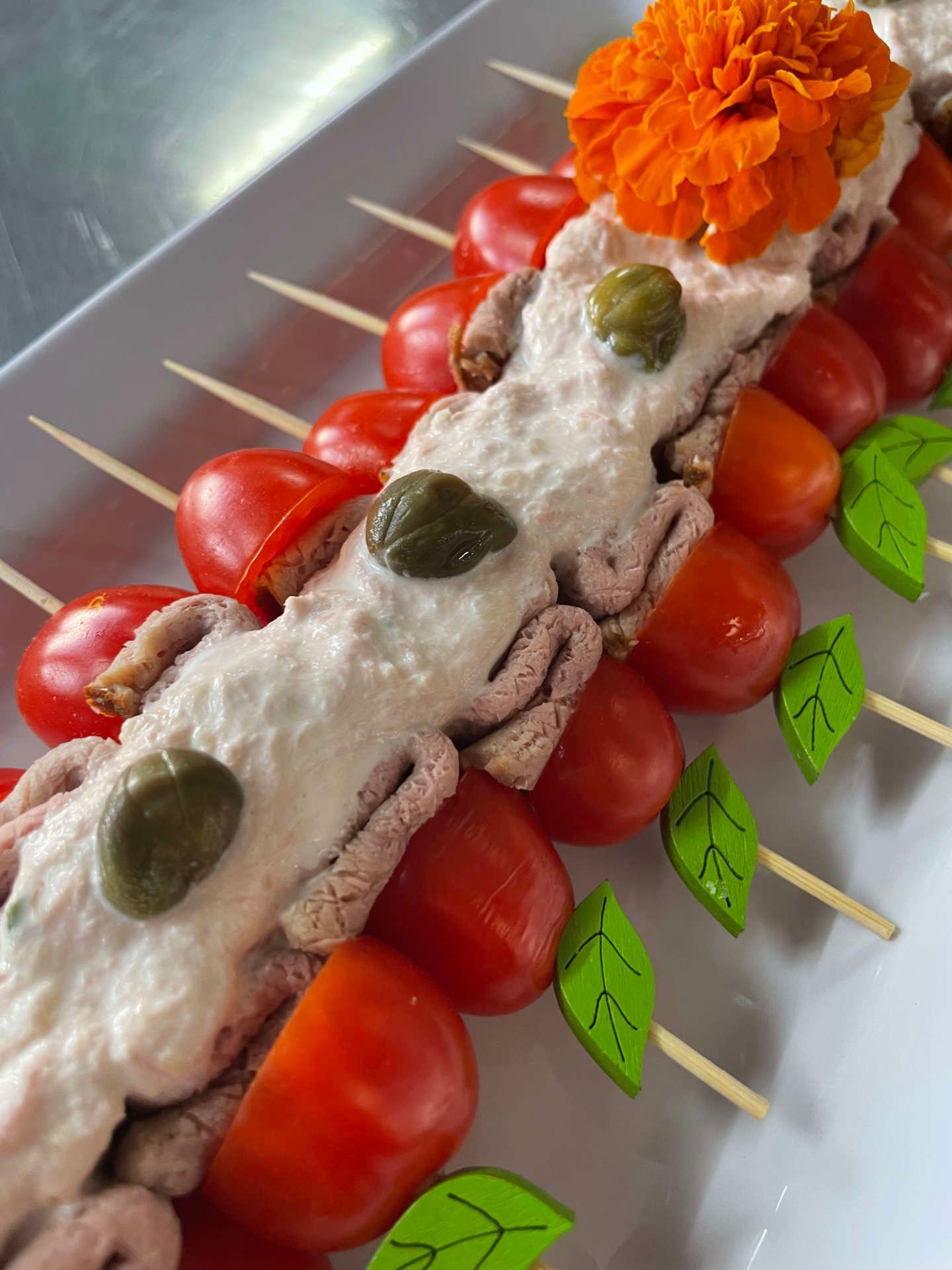 Ein weißer Teller, belegt mit Tomaten, Tintenfisch, Kapern und einer Blume.