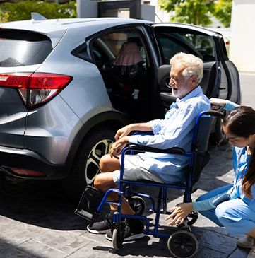 Une aide-soignante aidant un homme âgé handicapé à monter dans la voiture