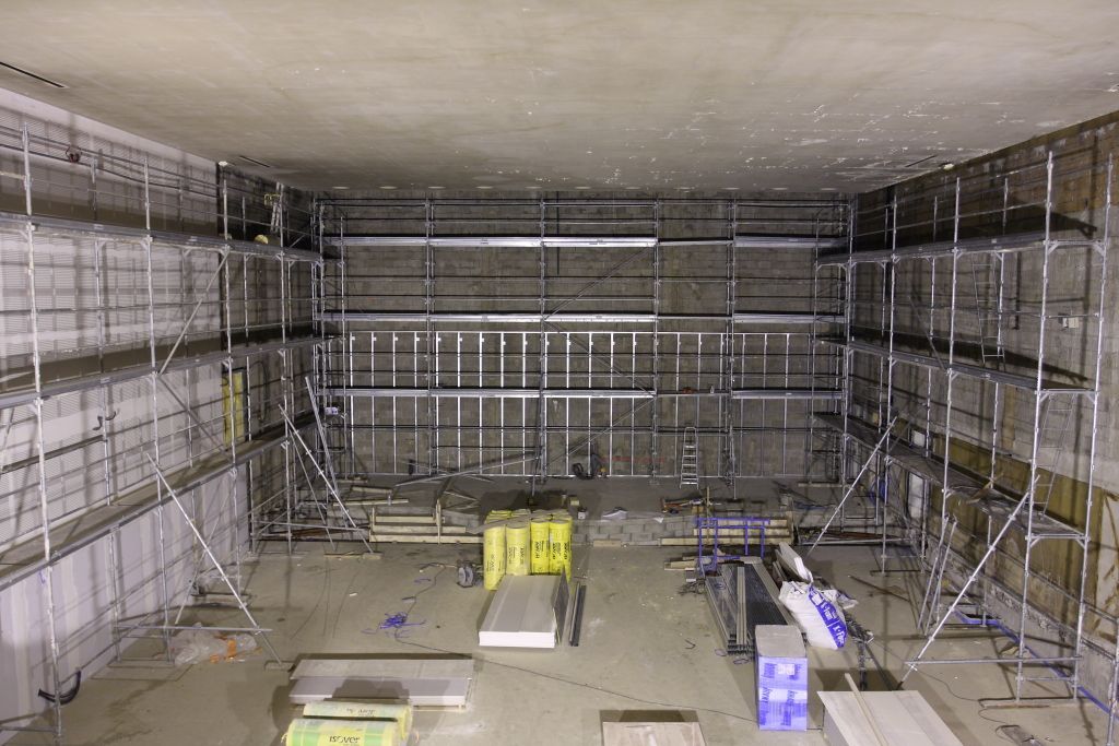 Chantier de construction avec murs bordés d'échafaudages, plafond en béton, matériaux au sol.