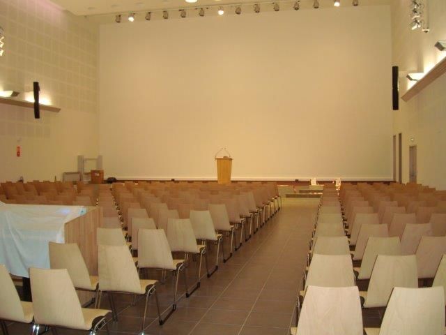 Auditorium avec des rangées de chaises faisant face à une scène équipée d'un podium et d'un écran blanc.