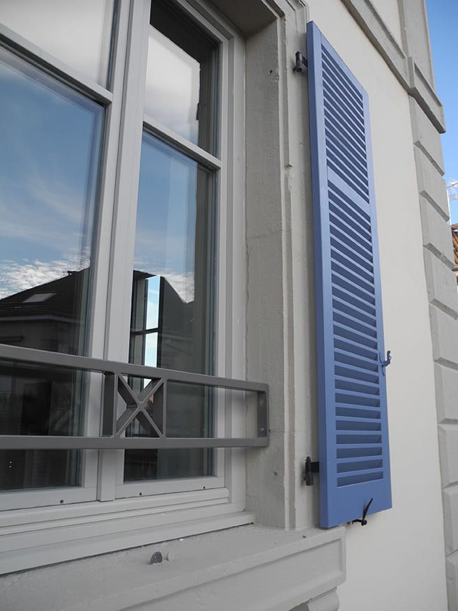 Fenêtre avec volets bleus et barre métallique décorative à l'extérieur.
