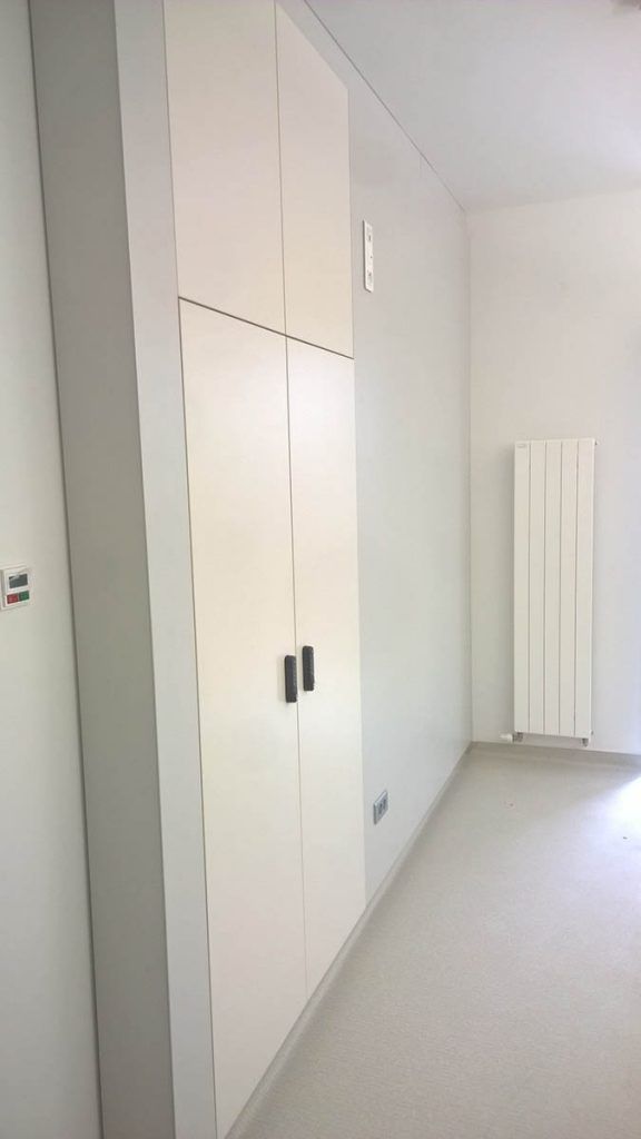 Placard encastré blanc haut avec poignées noires dans une pièce blanche, radiateur en arrière-plan.