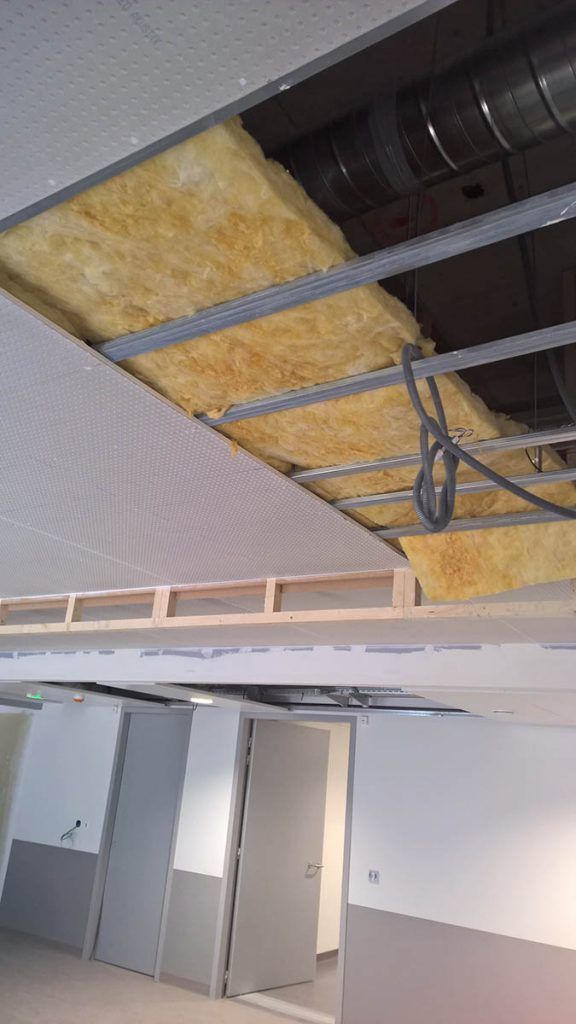 Vue intérieure d'un faux plafond ; isolation apparente, ossature métallique et conduits de ventilation visibles.