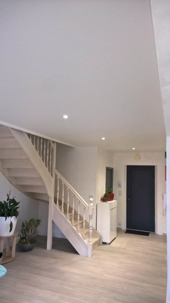 Un escalier blanc au sol clair mène à un plafond blanc. Une porte bleu foncé est visible.