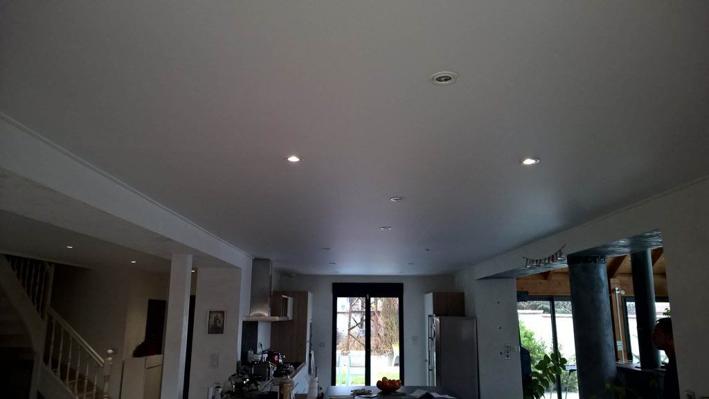 Vue intérieure d'un plafond blanc avec spots encastrés, au-dessus d'une cuisine avec placards, une fenêtre et un escalier.