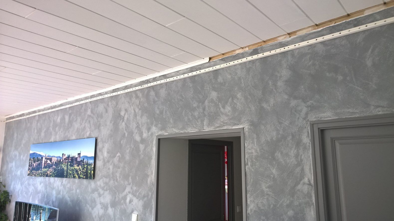 Mur gris texturé avec moulures et plafond blancs. Porte ouverte et porte fermée à droite. Œuvre d'art à gauche.