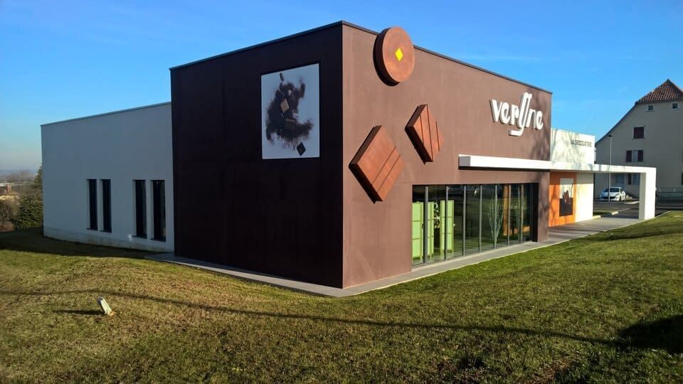 Boutique de chocolat avec façade marron et blanche, pelouse verte, ciel bleu.