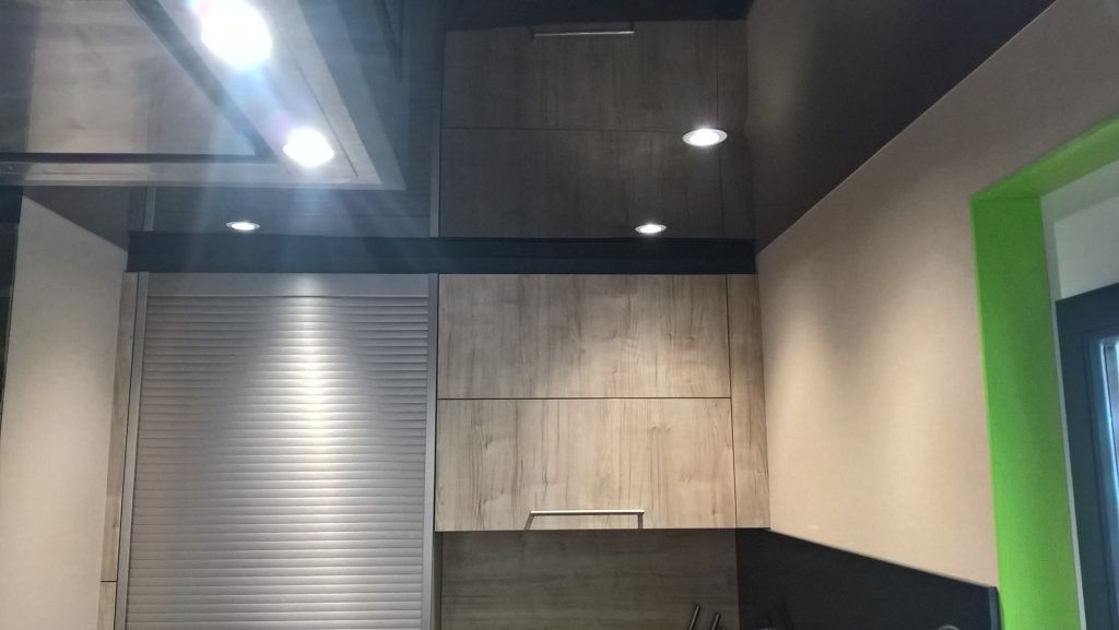 Intérieur de cuisine avec armoires foncées, stores en acier inoxydable et éclairage encastré lumineux.