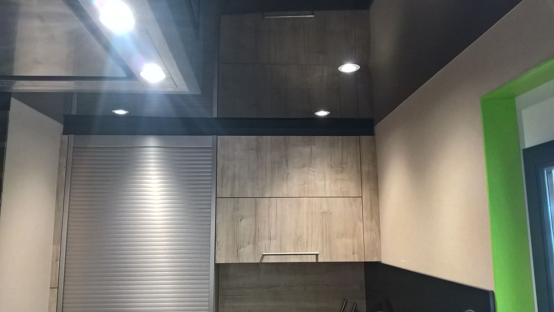 Cuisine avec placards en bois, porte sectionnelle en métal et éclairage encastré sur un plafond sombre.
