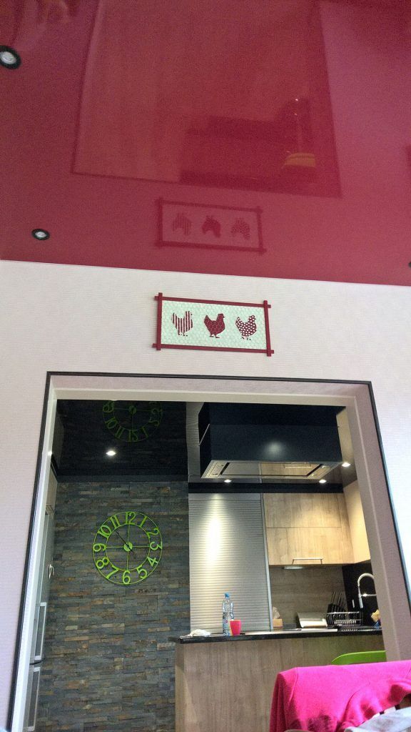 Une porte donne sur une cuisine. À gauche, un mur en pierres empilées orné d'une couronne verte.