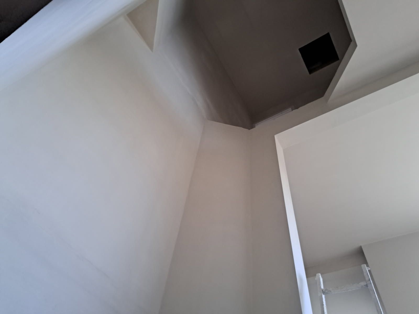 Angle intérieur d'un bâtiment aux murs blancs contrastant avec un plafond gris foncé, et une porte ouverte.