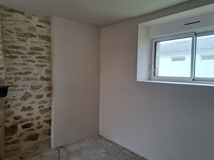 Pièce vide aux murs clairs, mur en pierres, une fenêtre avec des stores.