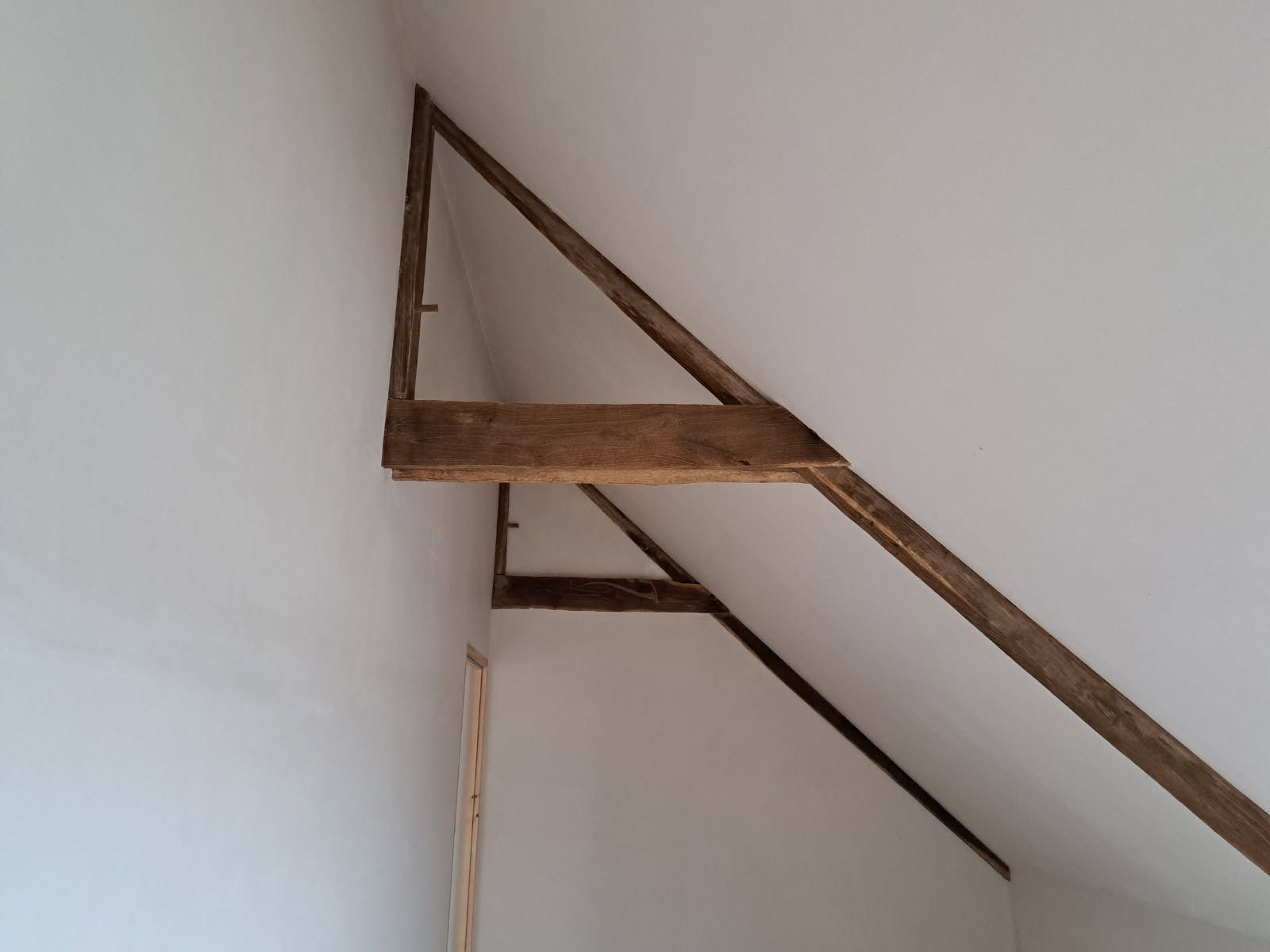 Des poutres en bois forment un triangle sur un mur blanc.