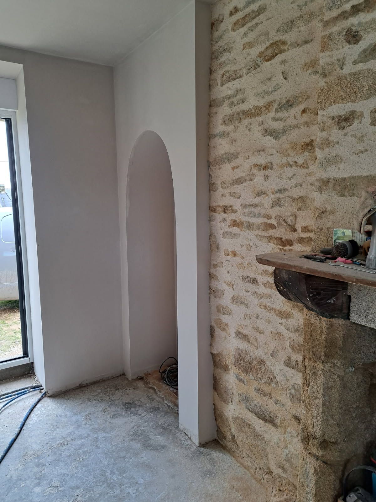 Intérieur avec mur en pierre, porte cintrée et mur peint en blanc à côté d'une fenêtre.