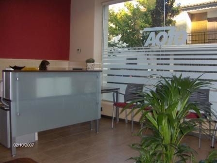 Área de recepción con escritorio gris, pared roja, sillas de espera y ventana esmerilada.