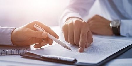 Manos señalando y escribiendo en un documento, posiblemente un contrato.