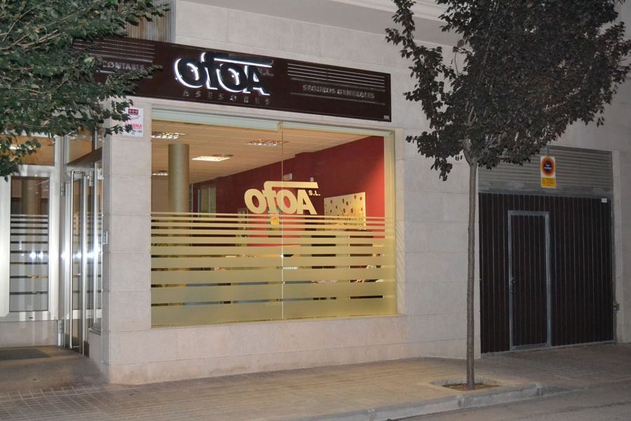 Exterior de la oficina de Otoa, con ventana de vidrio que muestra el logotipo, escaparate a la calle y puerta marrón.