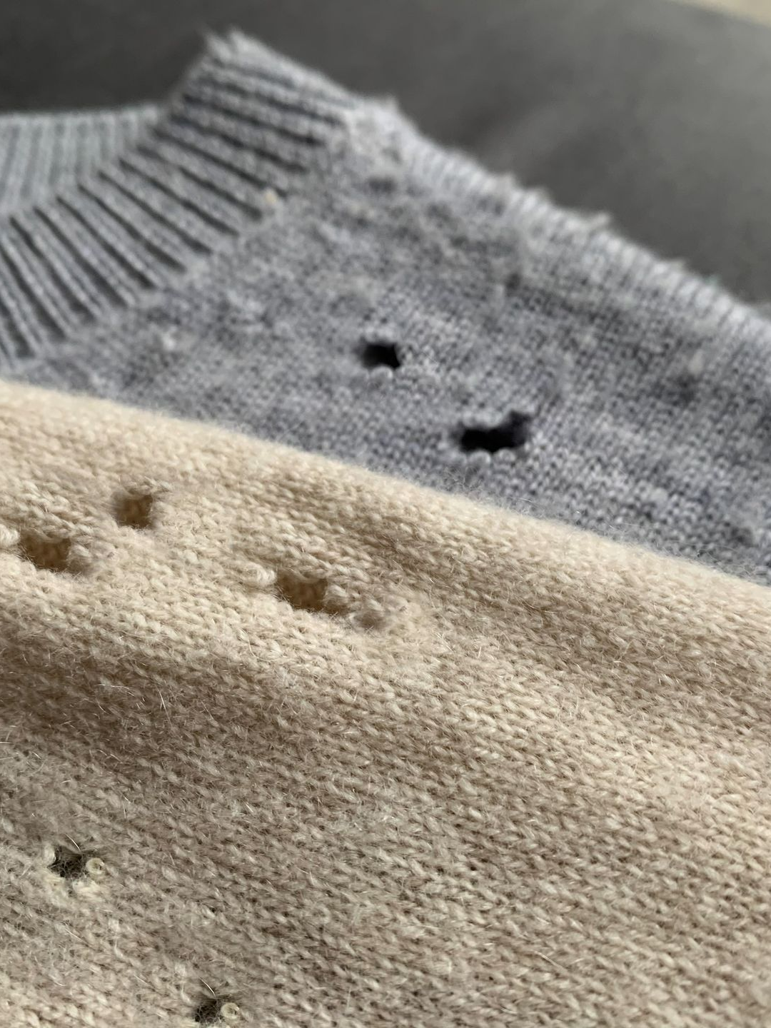 Gros plan de deux pulls de couleur claire, l'un gris, l'autre beige, tous deux avec de multiples trous.