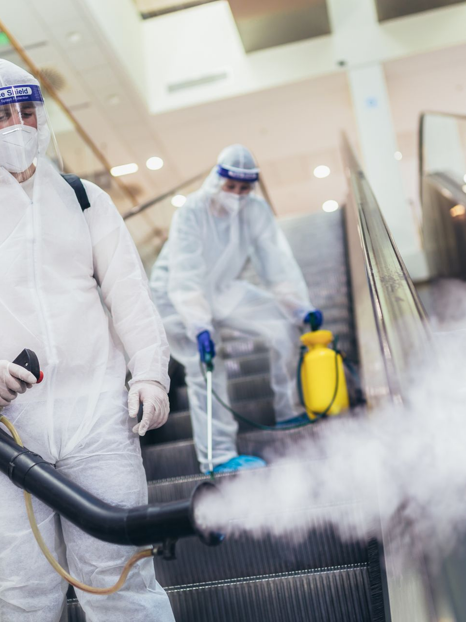 Des personnes en combinaison de protection désinfectent un escalator avec une machine à brouillard.