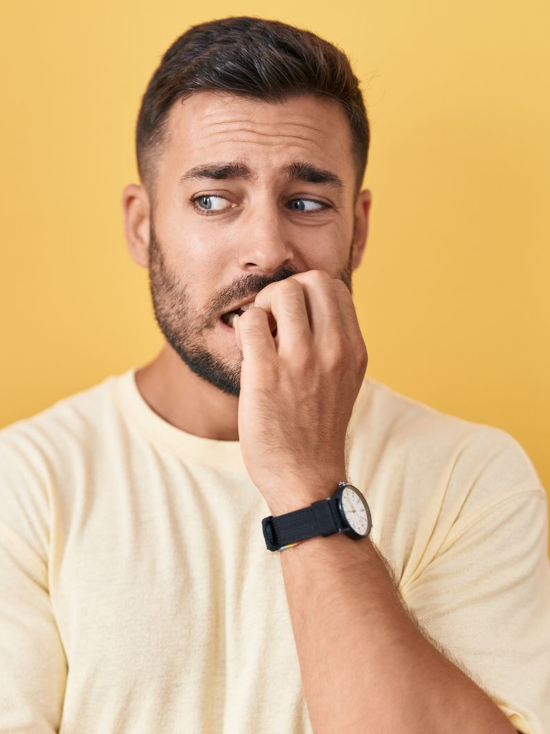 Homme se rongeant les ongles, l'air anxieux, sur fond jaune.