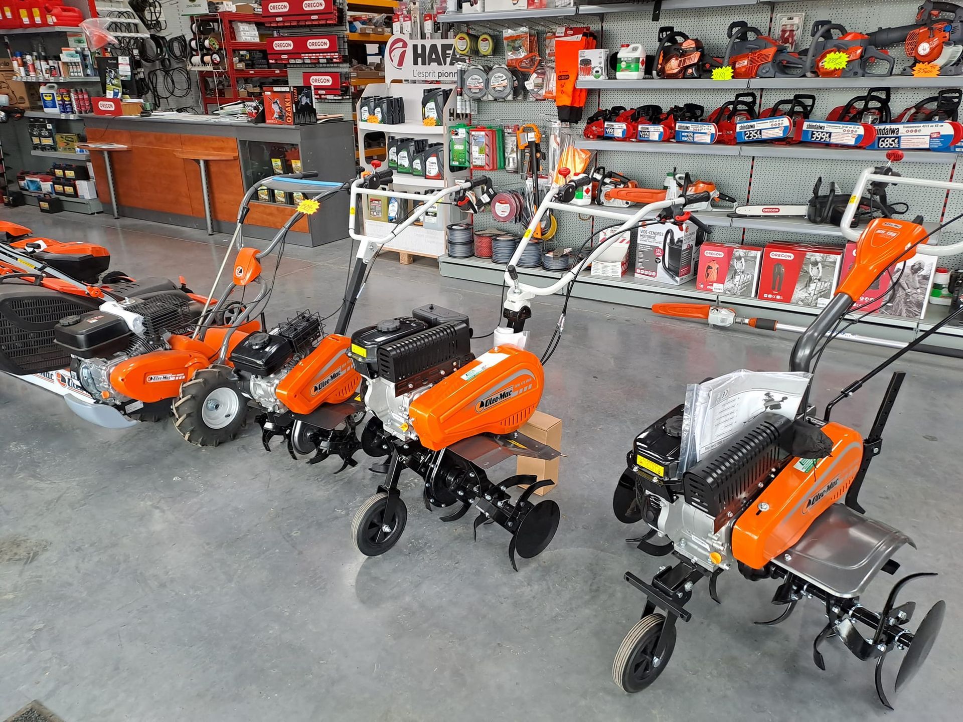 Rangée de motoculteurs orange exposés dans une quincaillerie. Rayons remplis d'outils en arrière-plan.