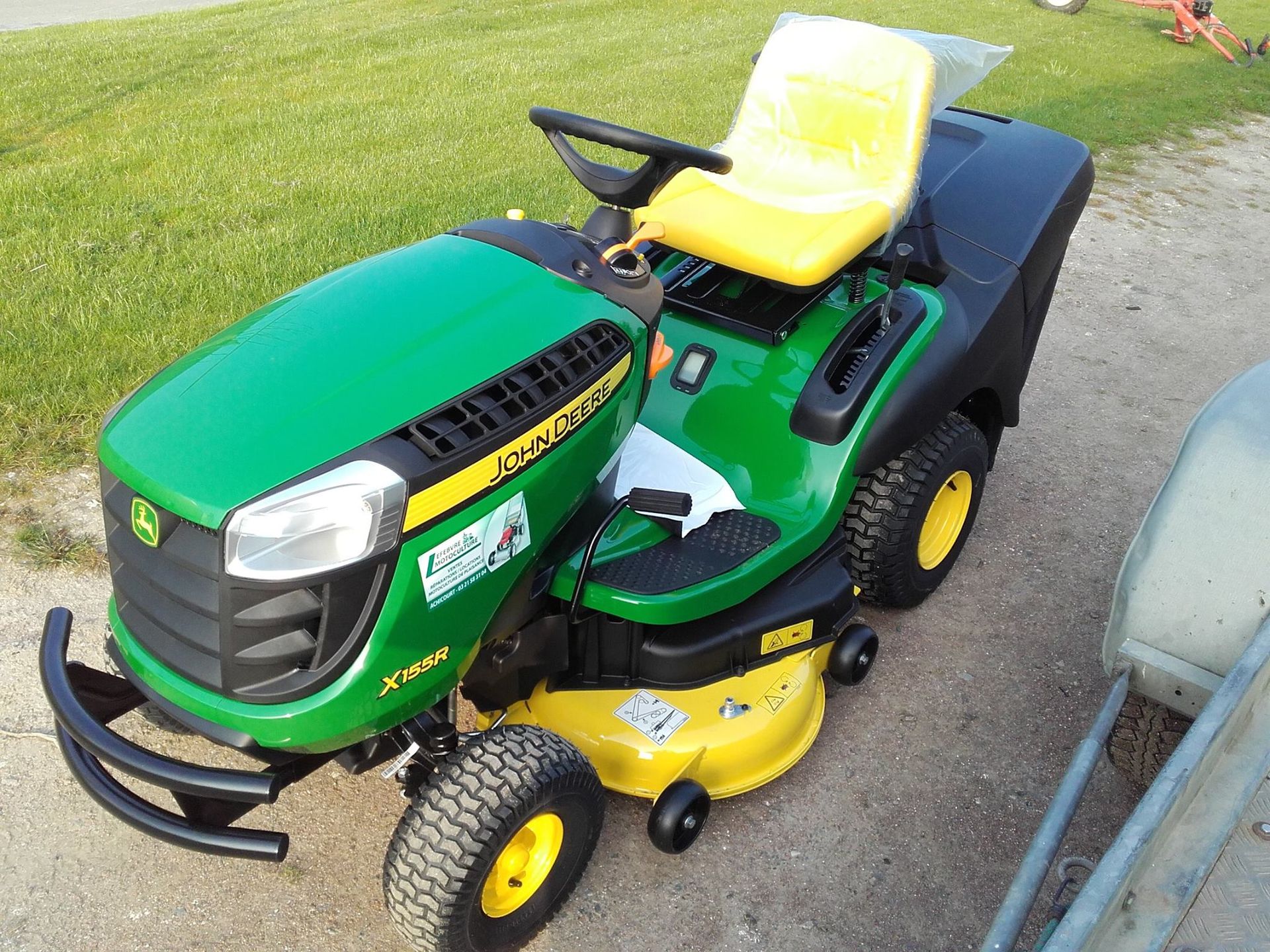 Tondeuse autoportée John Deere verte et jaune sur une allée de gravier, avec une pelouse verte en arrière-plan.
