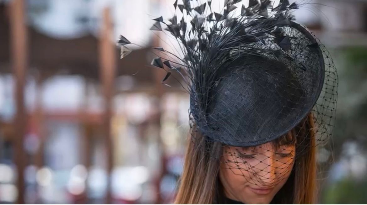 Mujer con tocado negro con plumas y velo facial; fondo borroso.