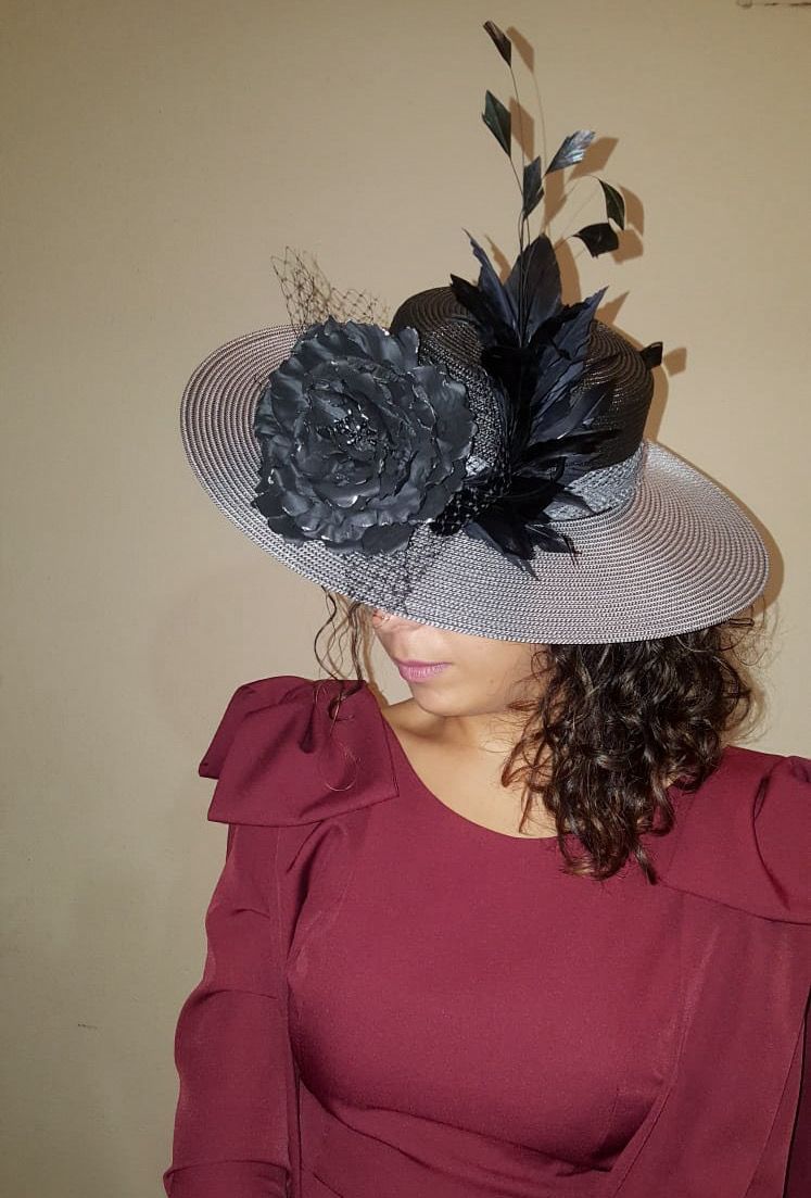 Mujer con top rojo y sombrero estampado con decoraciones florales y de plumas negras.