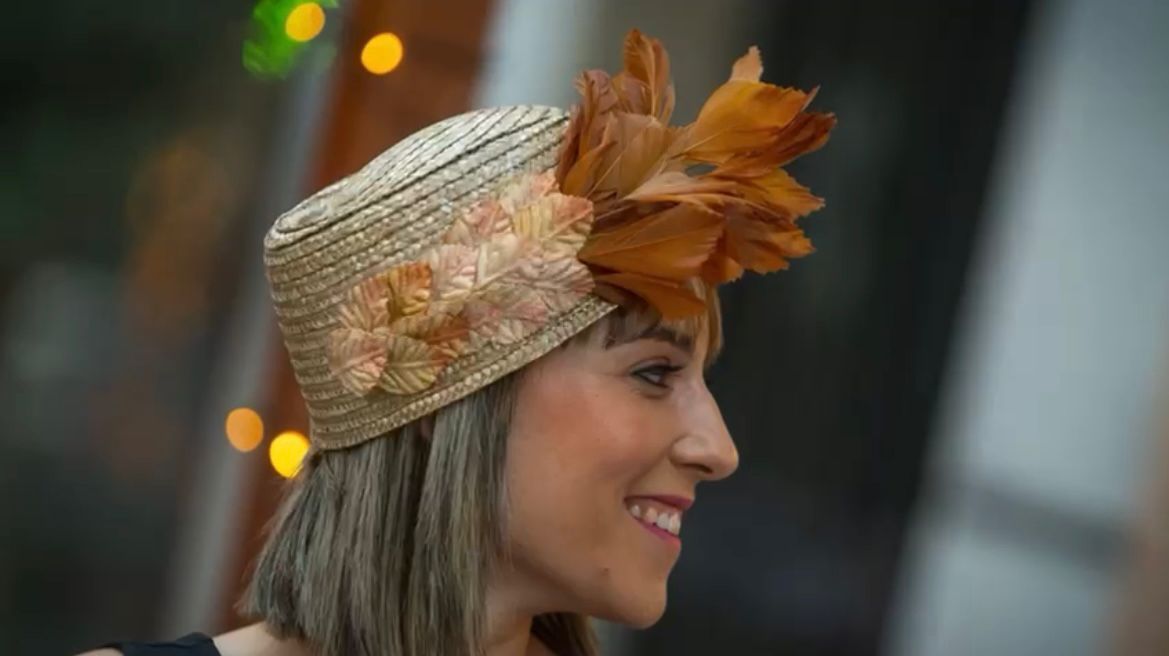Mujer con sombrero de paja adornado con plumas y adornos florales, sonriendo.