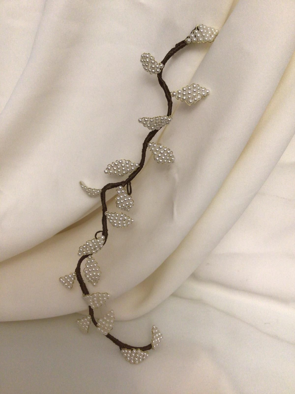 Un accesorio para el cabello con forma de enredadera con hojas que parecen perlas sobre una tela blanca.