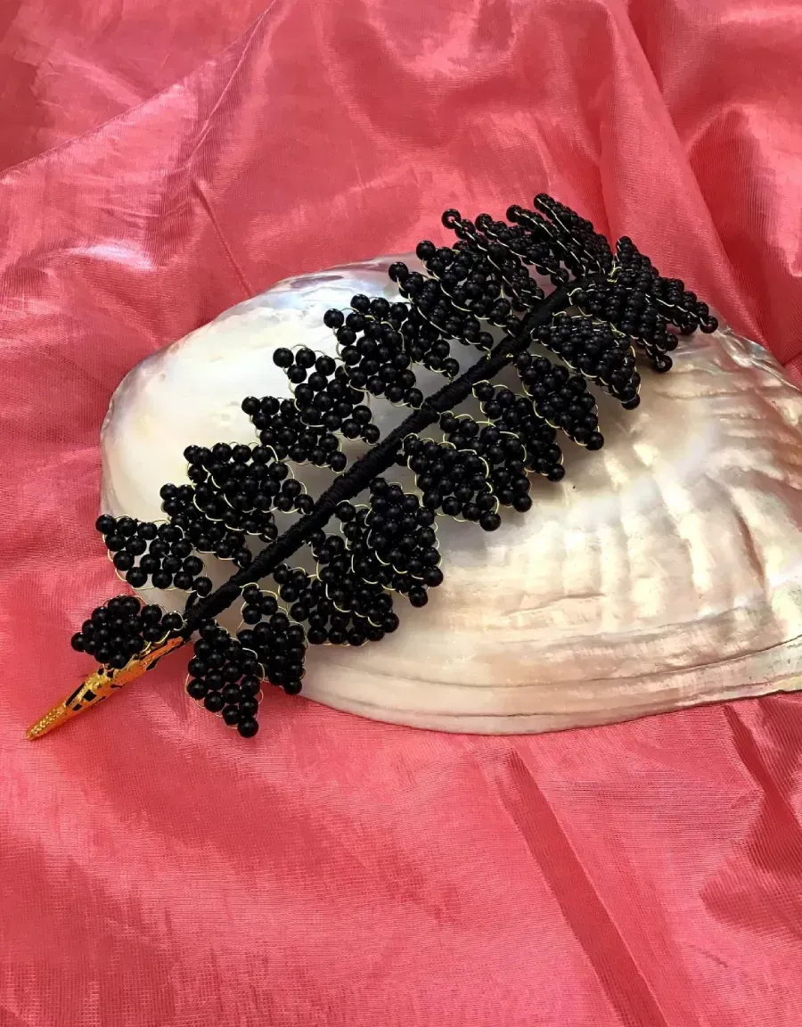 Accesorio para el cabello hecho con hojas y cuentas negras sobre una concha, sobre una tela rosa.