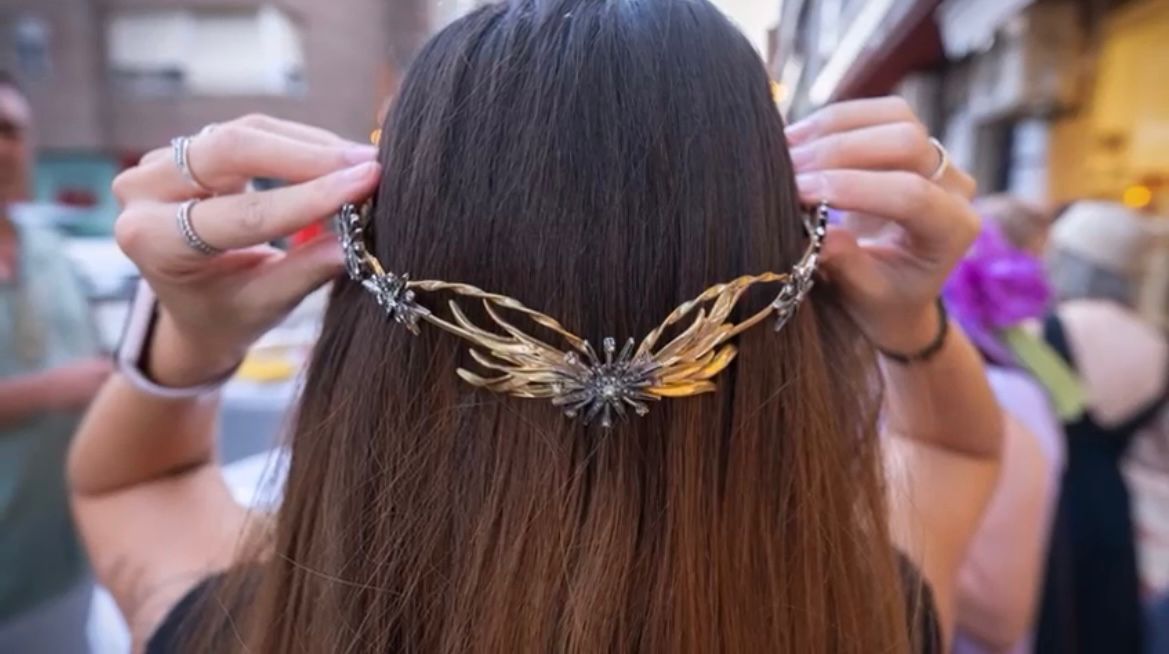 Mujer poniéndose un tocado de oro y plata con diseño en forma de ala, al aire libre.