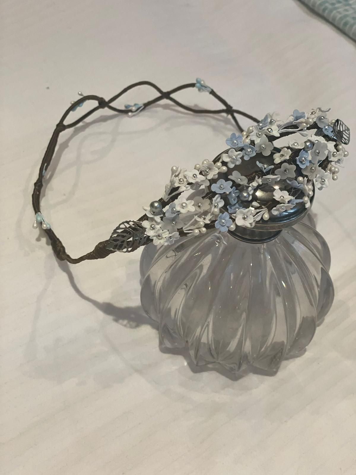 Una delicada corona floral con detalles en azul y blanco reposa sobre una botella de vidrio decorativa.