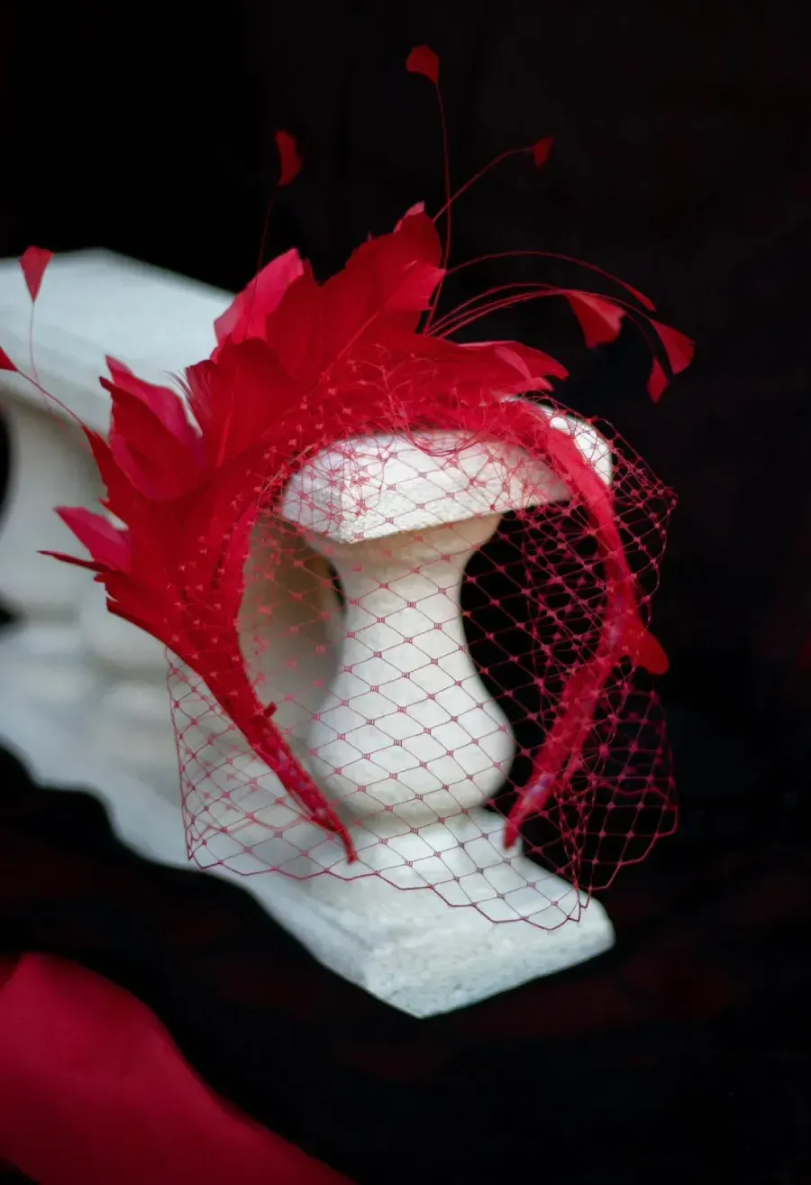 Diadema de plumas rojas con velo sobre pedestal blanco.