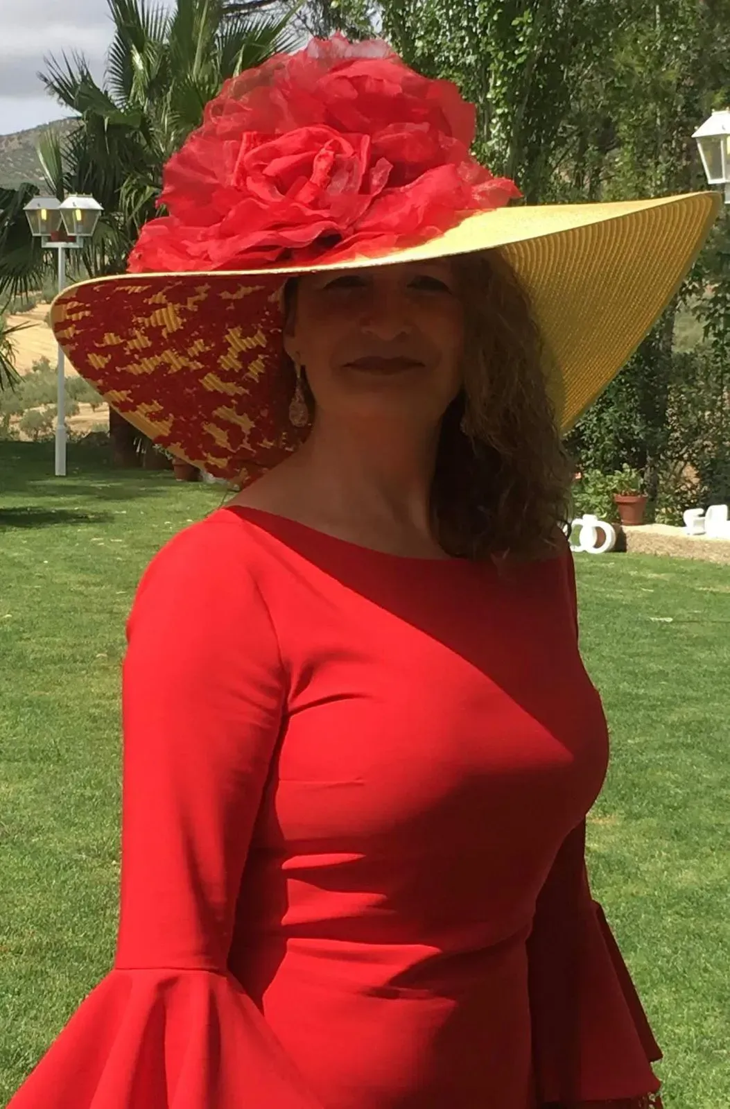 Mujer con un vestido rojo y un sombrero grande con un acento floral rojo, de pie afuera.