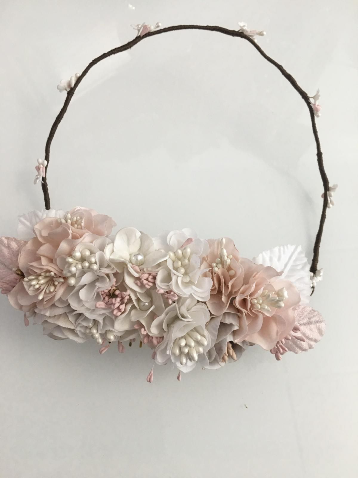 Corona de flores con flores blancas, rosas y marfil sobre una base de alambre marrón.